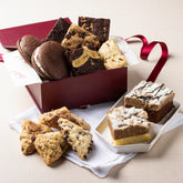 Assorted cookies and brownies in a gift box with a red ribbon on a beige surface.