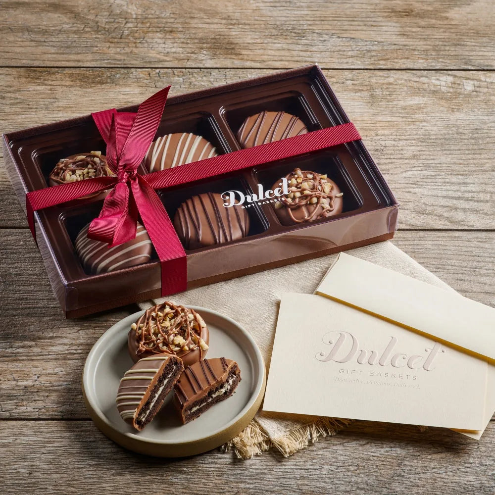 Dulcet gift box of chocolate dipped OREO cookies tied with a red ribbon, with more dipped cookies on a plate