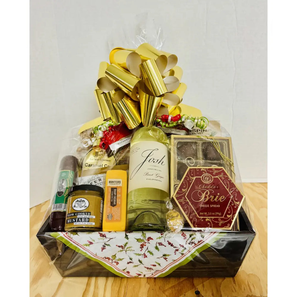 Gift basket with wine, cheese, and other items on a wooden surface.